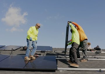 Three workers dressed in yellow installing solar panels on a rooftop